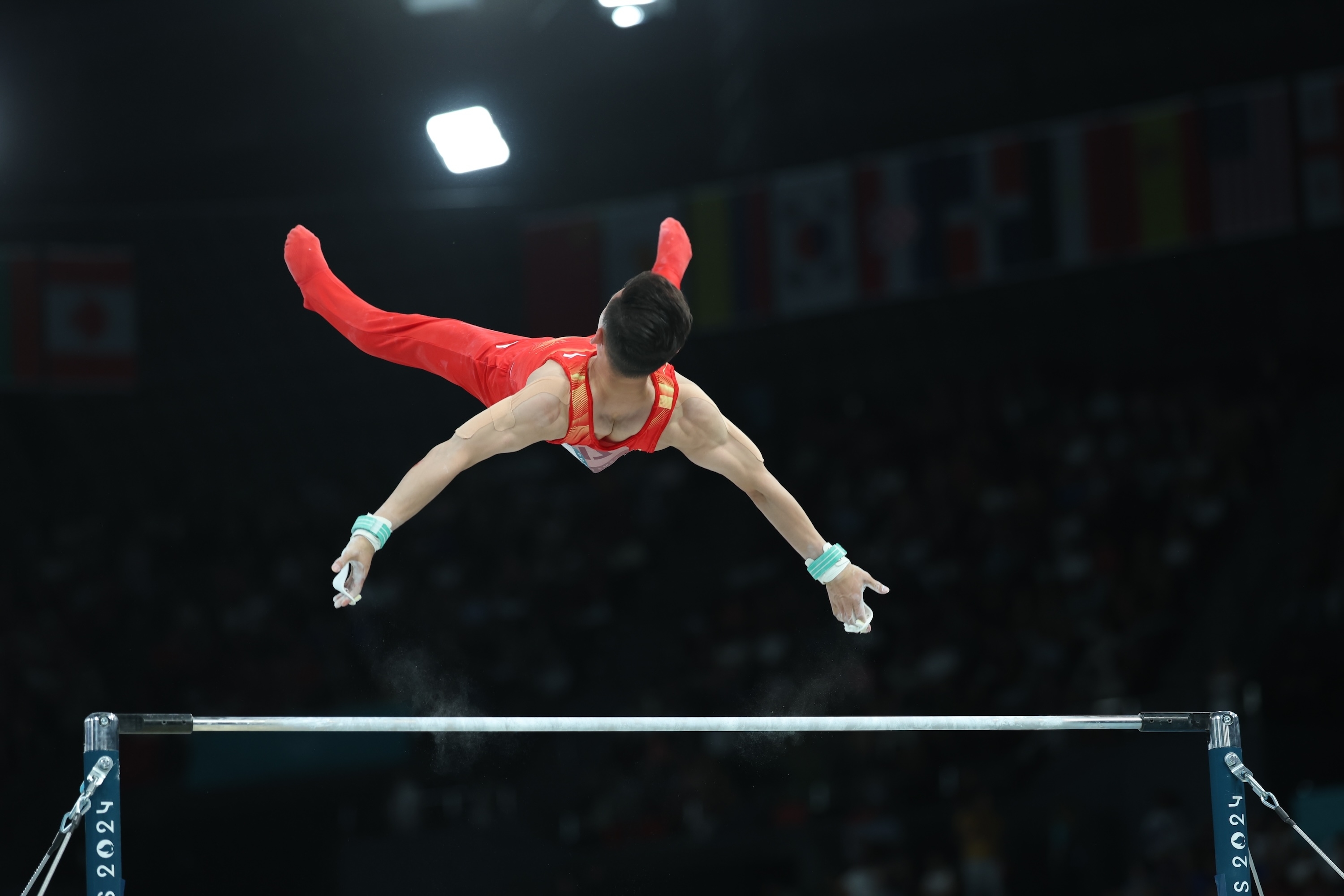 Gymnast in mid-air executing a move on the horizontal bar during a competition