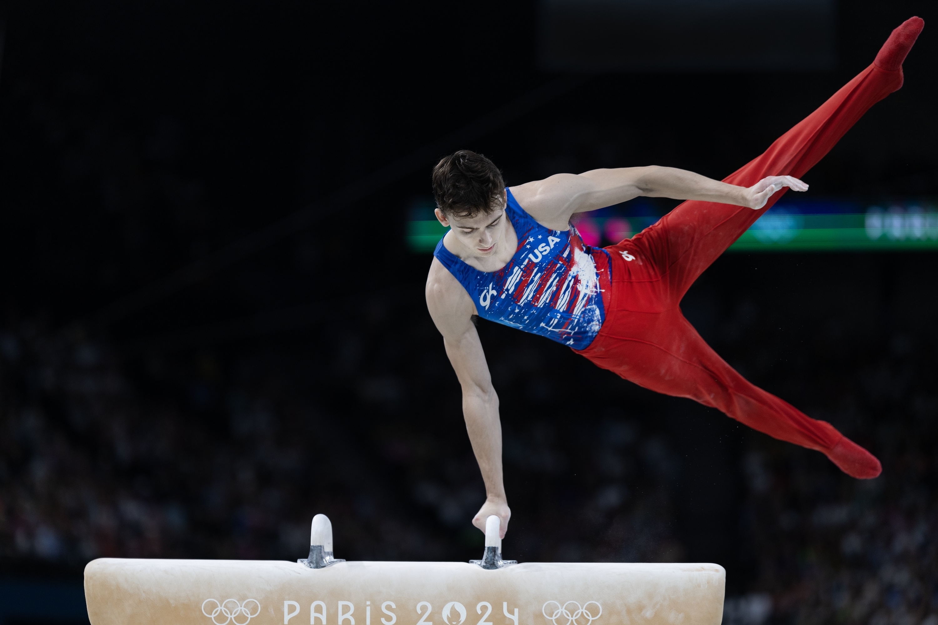 Male gymnast performing a pommel horse routine, wearing a sleeveless uniform with USA lettering, at the Paris 2024 Olympics