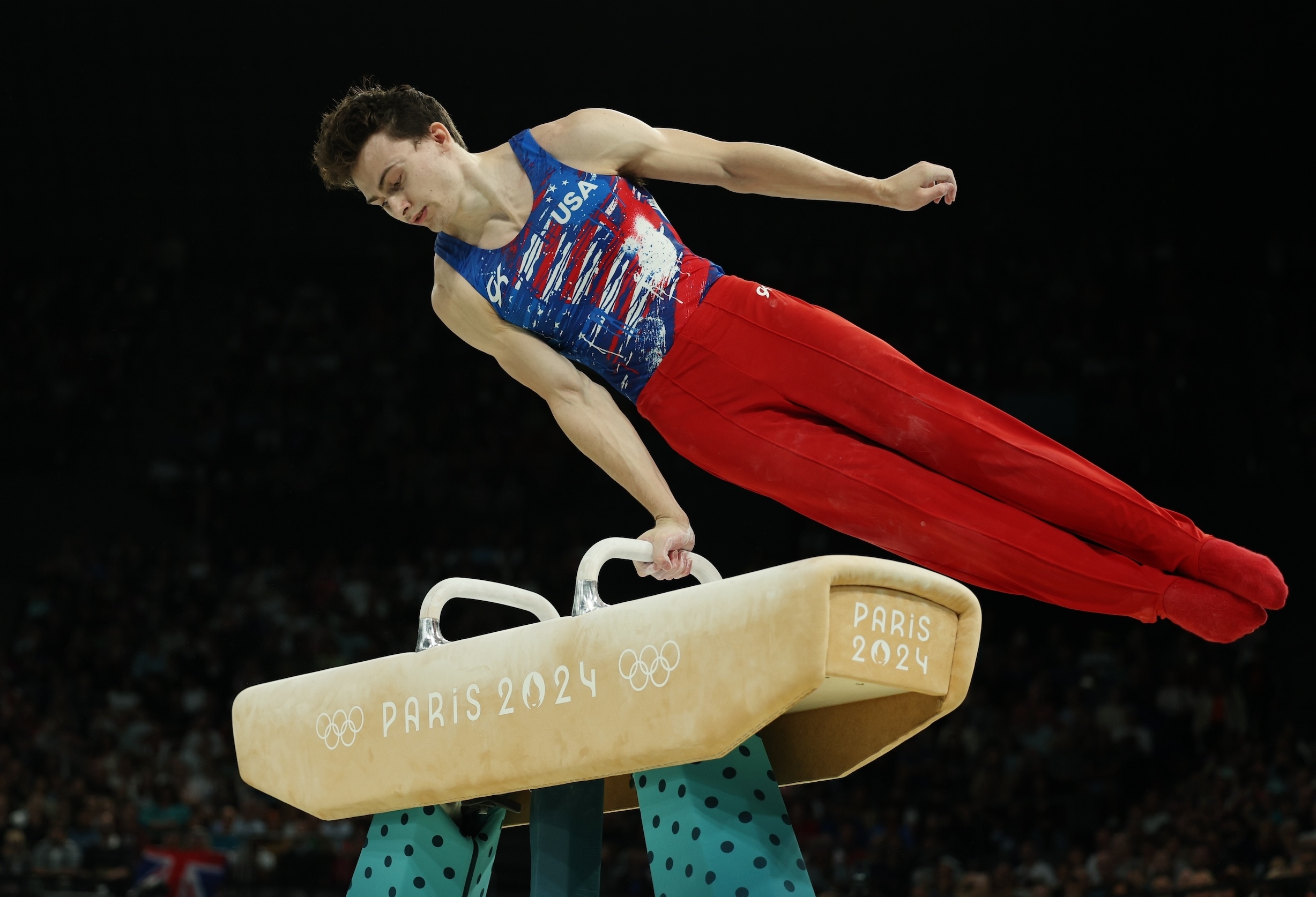 An athlete in red pants and USA top performs a pommel horse routine at the Paris 2024 Olympics