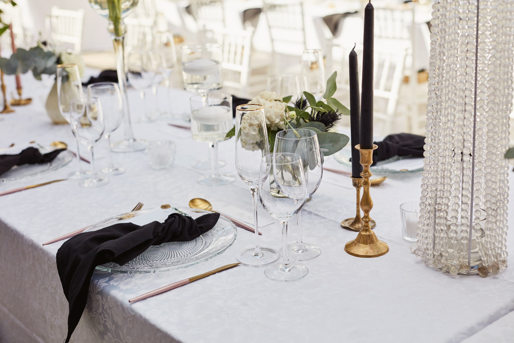 Elegant table setting with black napkins, crystal glassware, gold utensils, and floral centerpieces arranged for a formal event