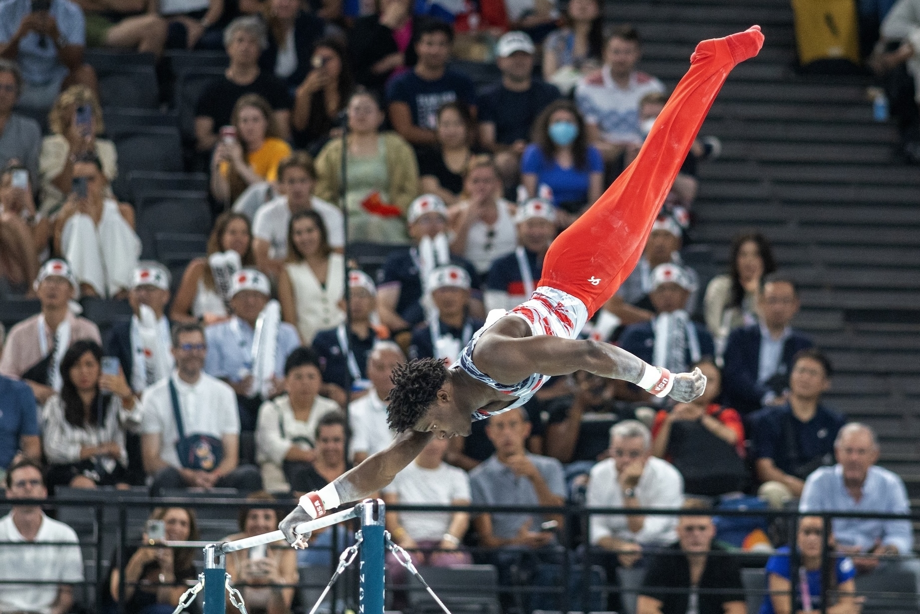 Simone Biles performs a handstand on the uneven bars during a gymnastics competition, with the audience watching intently