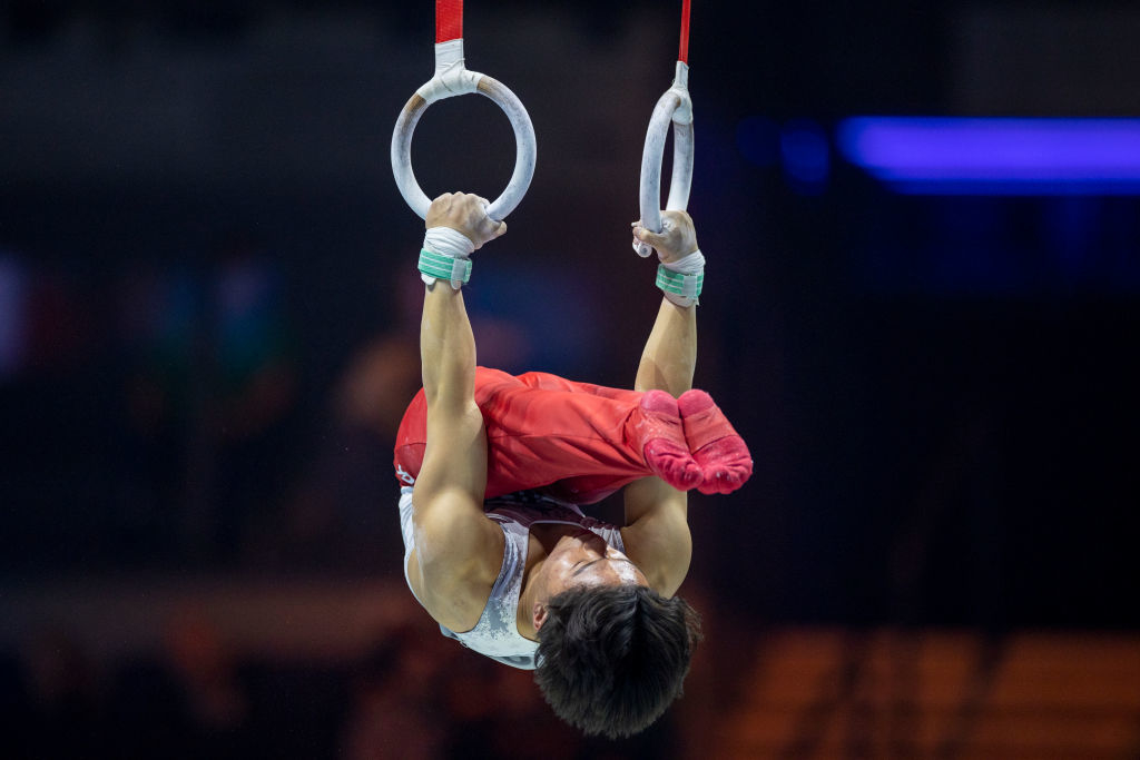 A gymnast performs an iron cross on rings during a competition. The athlete's face is not visible