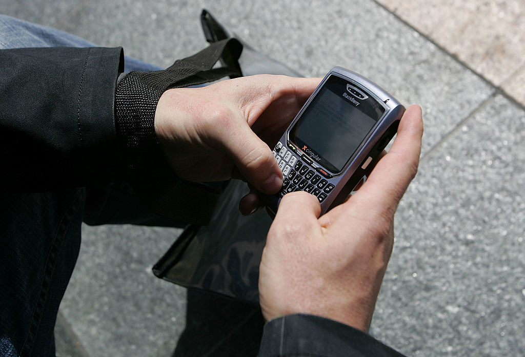 Close-up of a person's hands holding an older model Blackberry phone with a physical keyboard, typing a message