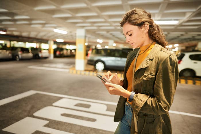 A woman stands in a parking garage, using her phone