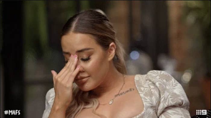 A woman with a tattoo on her chest and wearing a floral-patterned dress wipes her eye with her fingers. Hashtag #MAFS is in the lower-left corner