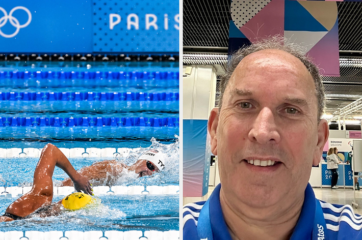 男性が「PARIS 2024」と書かれたバナーの前でセルフィーを撮っています。彼は青いシャツを着ています。