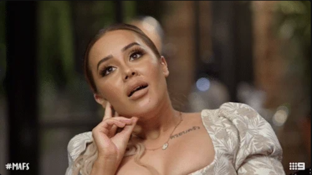 Woman from "Married at First Sight" (MAFS) in a patterned dress, looking up with her hand near her face