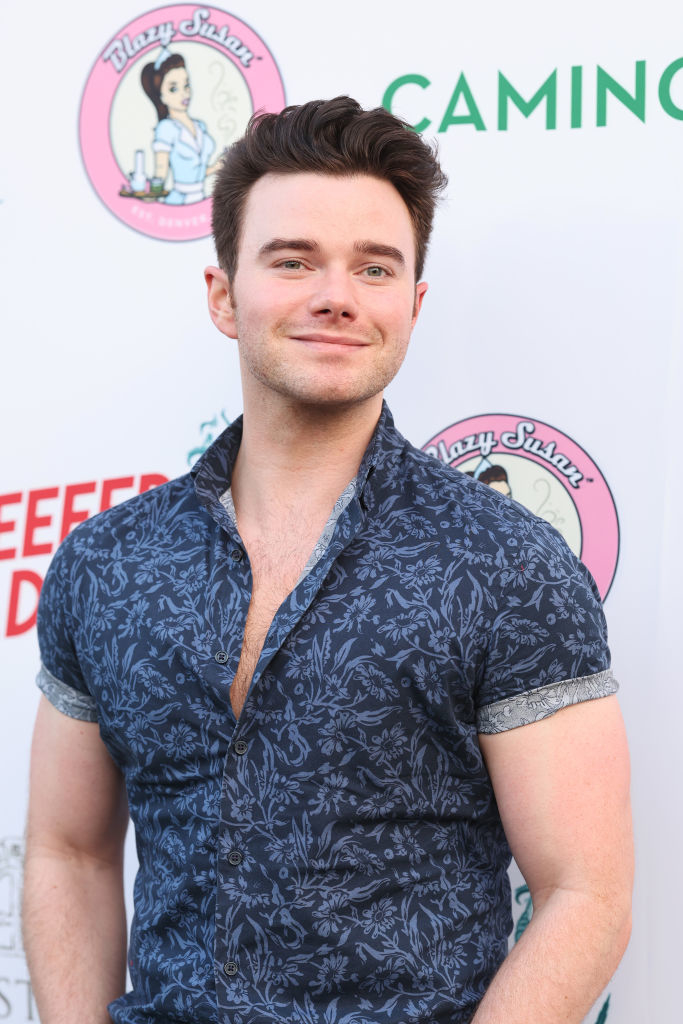 Chris Colfer at a red carpet event, wearing a short-sleeve, button-up shirt with a floral pattern