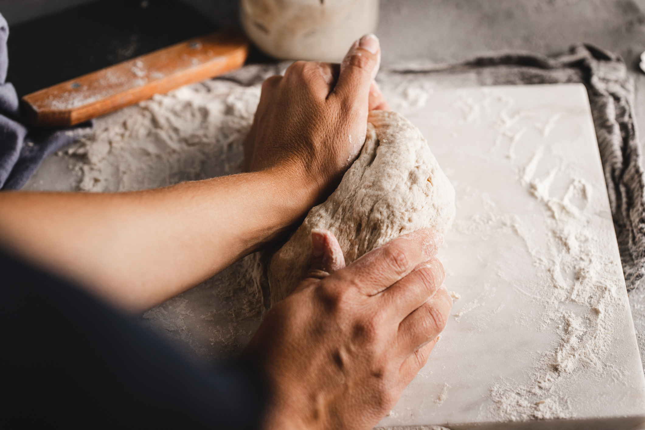 Two hands kneading dough on a floured surface