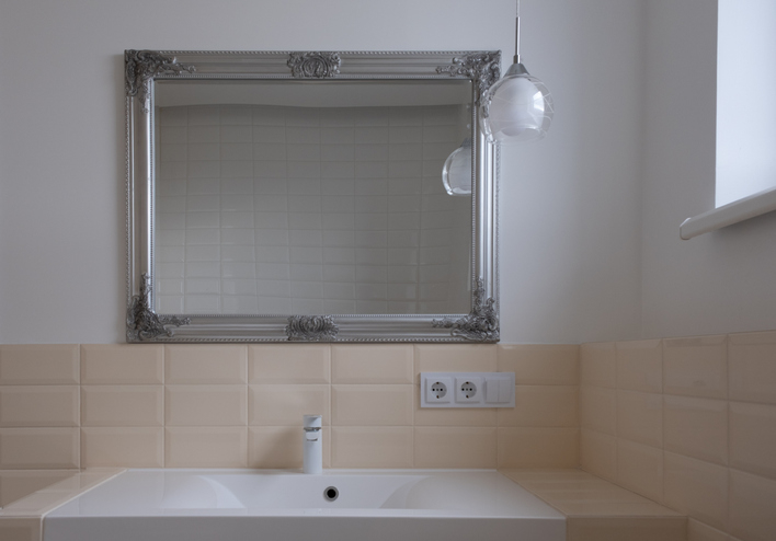 Bathroom with a large rectangular mirror above a sink and faucet, beige tiled wall, and a pendant light hanging beside the mirror