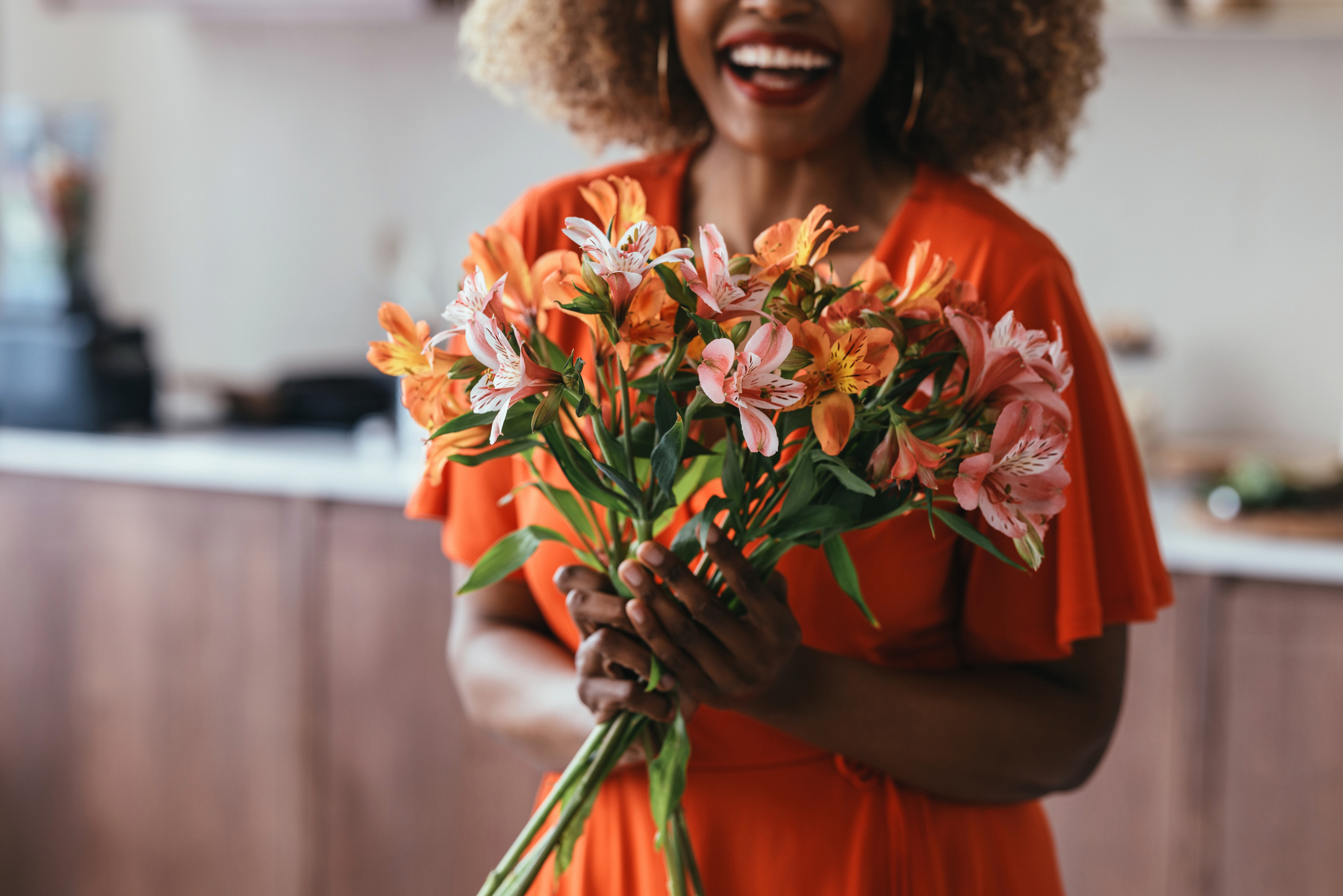 Woman smiling and holding a colorful bouquet of flowers in the kitchen