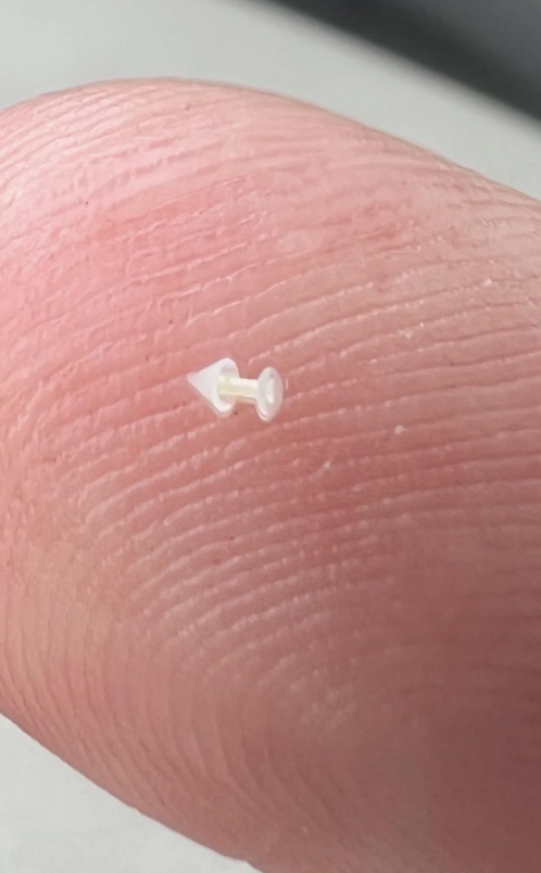 A close-up of a fingertip holding a very small, clear microchip