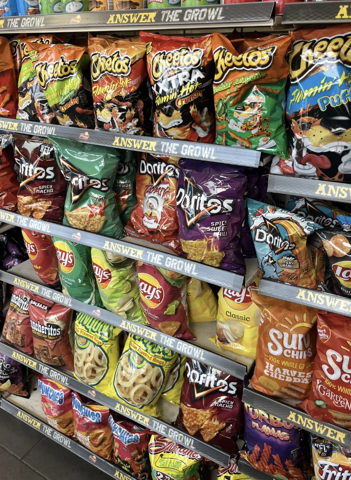 Various snack bags, including Cheetos, Doritos, Lay's, Sun Chips, and Munchies, neatly arranged on shelves with &quot;ANSWER THE GROWL&quot; signage