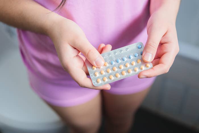 Person in a casual outfit holding a pack of birth control pills in their hands