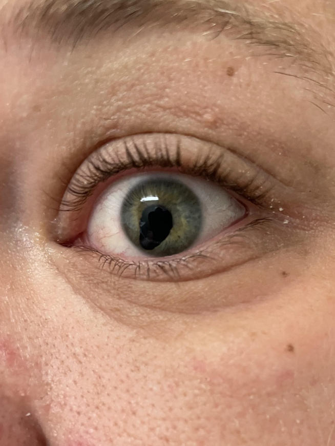 Close-up image of a person's eye, highlighting a wide-open green iris and visible eyelashes