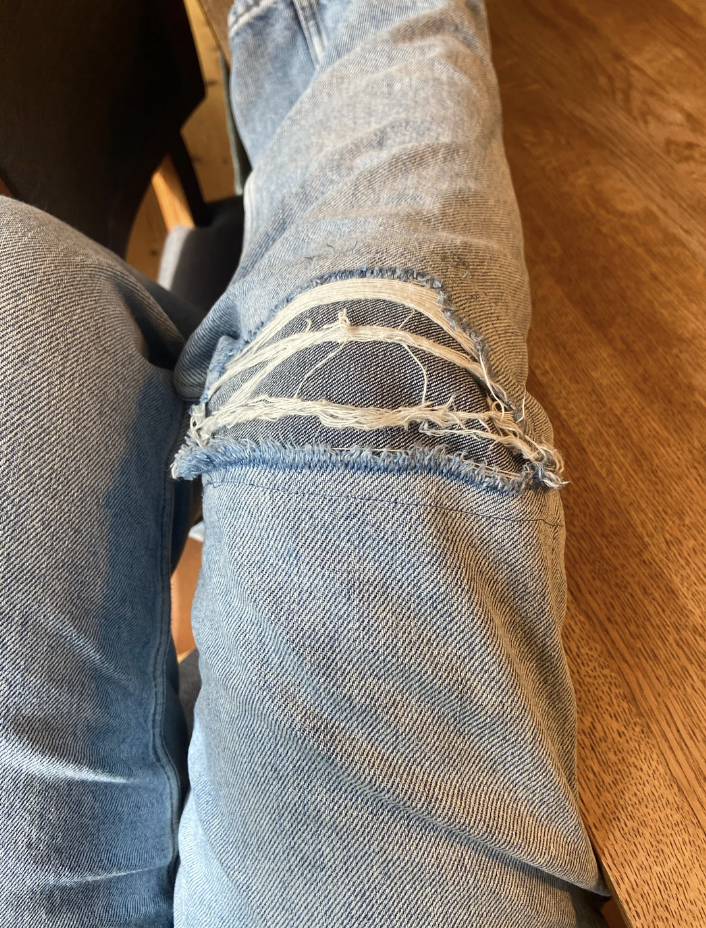 Ripped blue denim jeans showing a close-up of the knee area with frayed and torn fabric