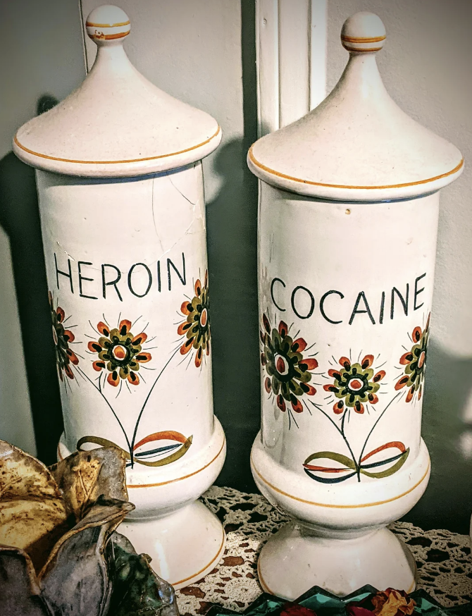 Two vintage apothecary jars labeled "Heroin" and "Cocaine" with floral decorations are displayed together