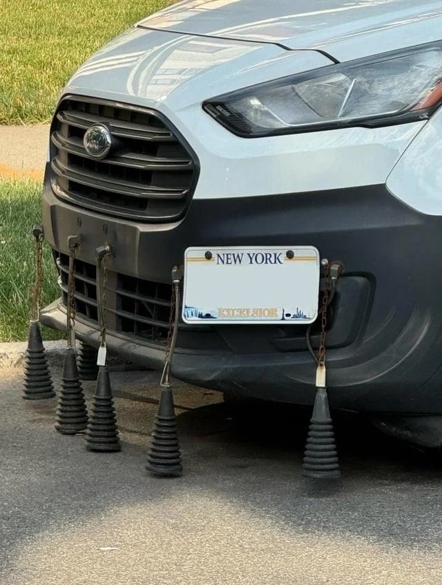 Front of a car with a New York license plate mounted on the bumper along with five ribbed cone-shaped objects hanging underneath