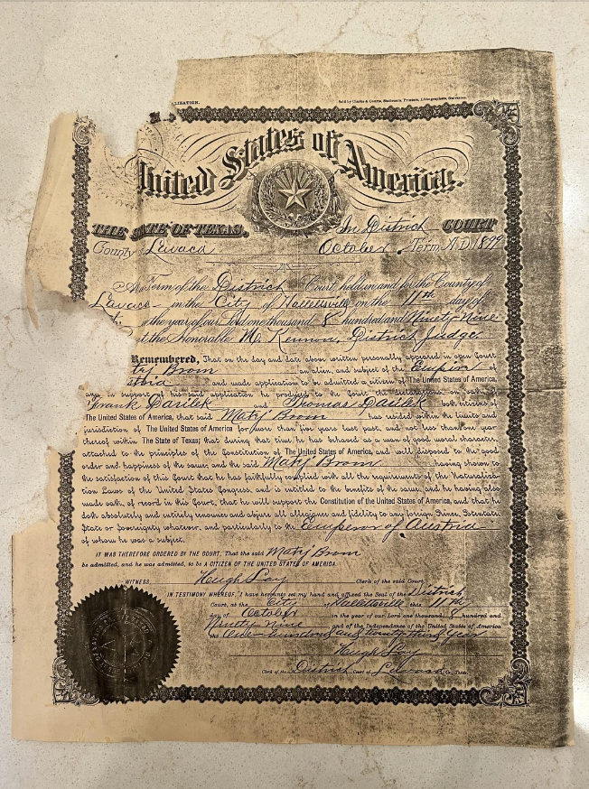 An old, partially damaged document from 1910 titled "United States of America" appears to be a Certificate of Citizenship issued by the U.S. District Court