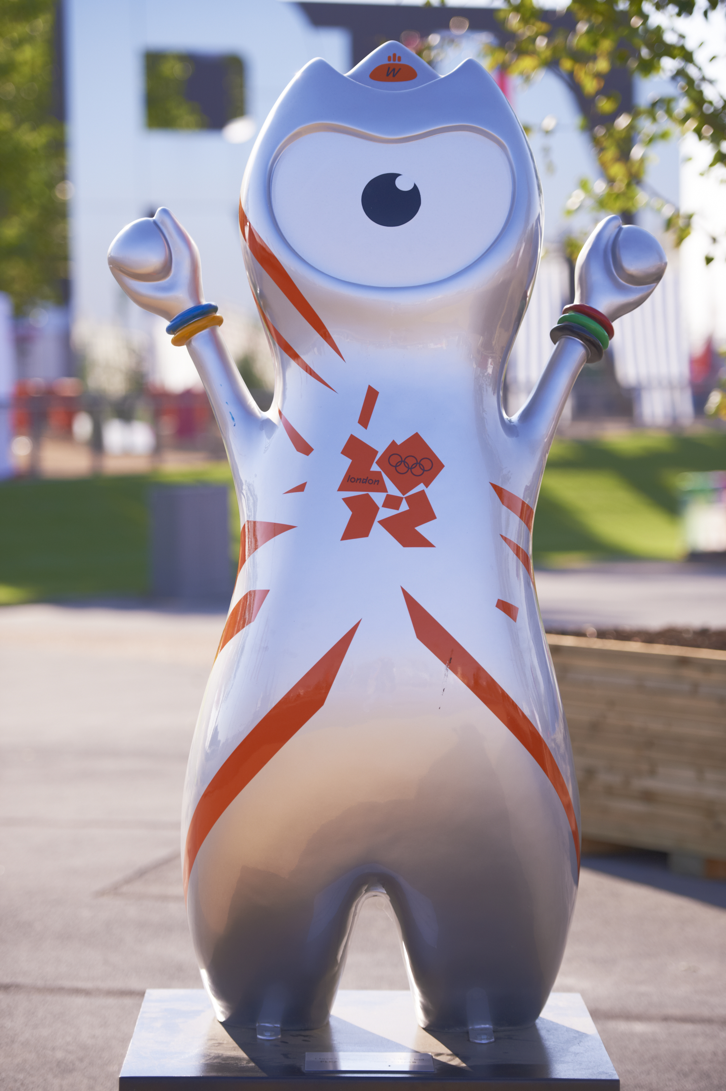 Wenlock, the silver mascot of the 2012 London Olympics, is standing with arms raised. The statue has a single large eye and orange Olympic symbols