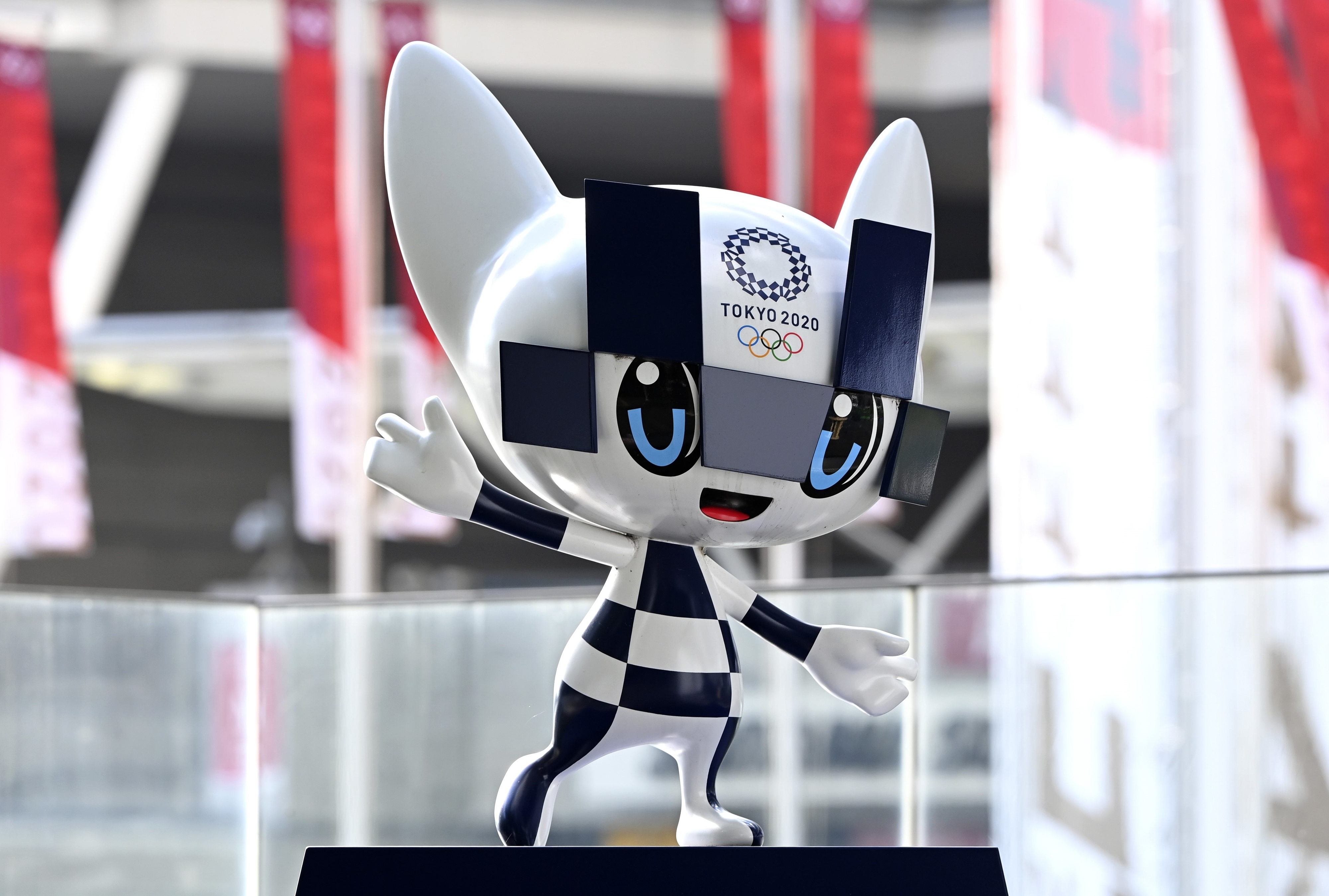 Miraitowa, the mascot for the Tokyo 2020 Olympics, is waving. The character features large eyes, a futuristic design, and is blue and white