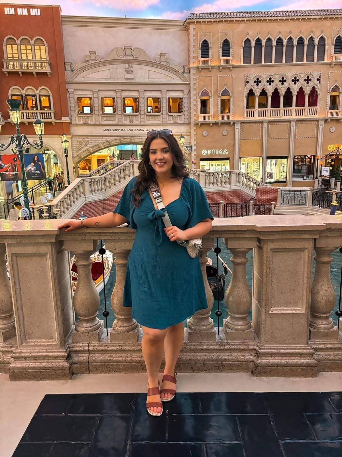 reviewer wearing the blue dress and sandals stands near a balcony overlooking a Venice-inspired shopping area