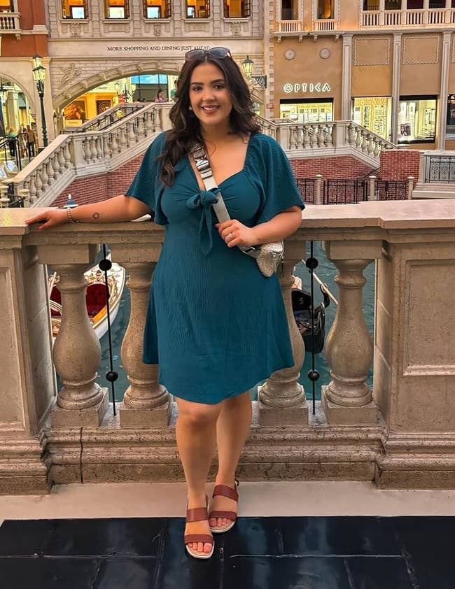 reviewer wearing the blue dress and sandals stands near a balcony overlooking a Venice-inspired shopping area