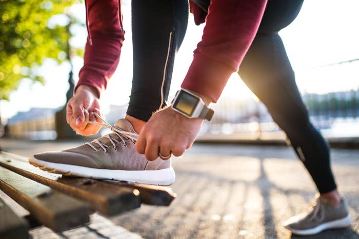 Person in athletic wear tying their running shoe while resting one leg on a bench beside a waterfront