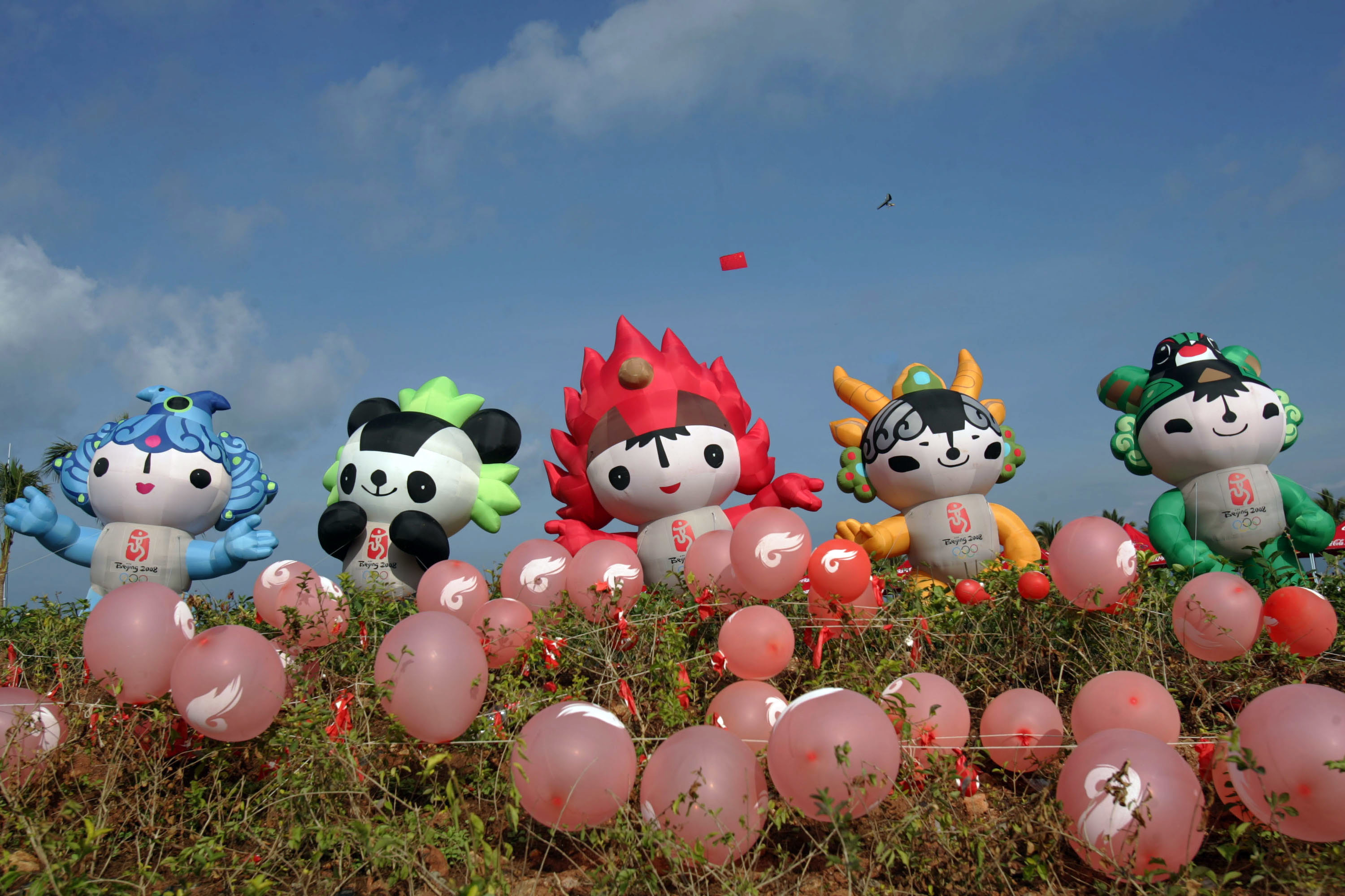 Inflatable mascots from the 2008 Beijing Olympics, Beibei, Jingjing, Huanhuan, Yingying, and Nini, are displayed among red balloons on a grassy hill