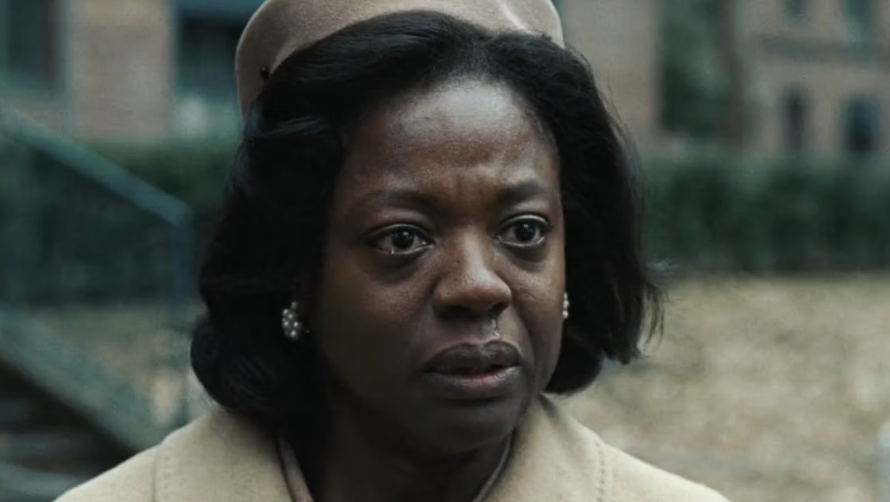 Viola Davis, wearing a coat and beret, has a serious expression and appears to be in an outdoor setting