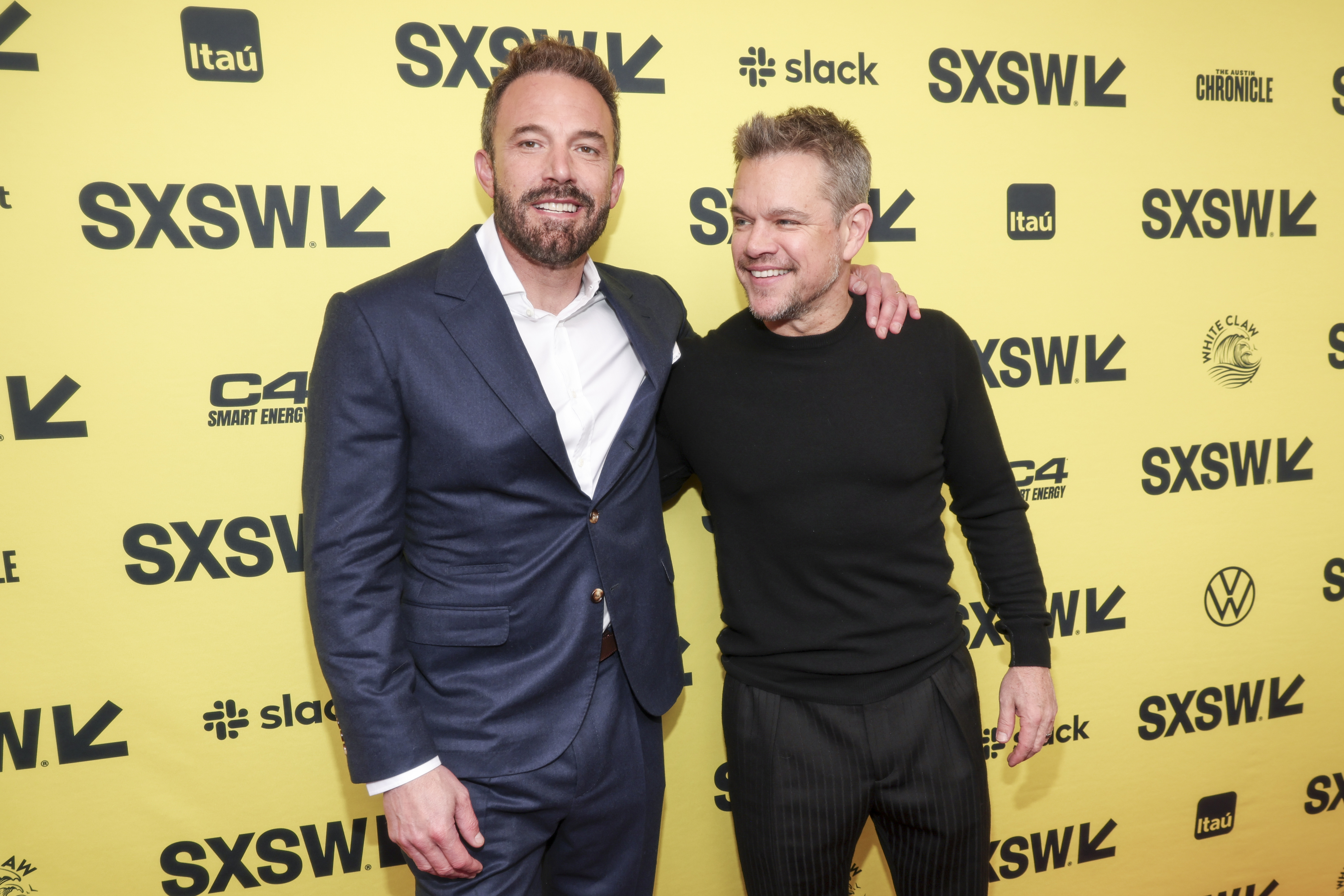 Ben Affleck in a suit and Matt Damon in a black sweater and trousers, posing together at the SXSW event backdrop
