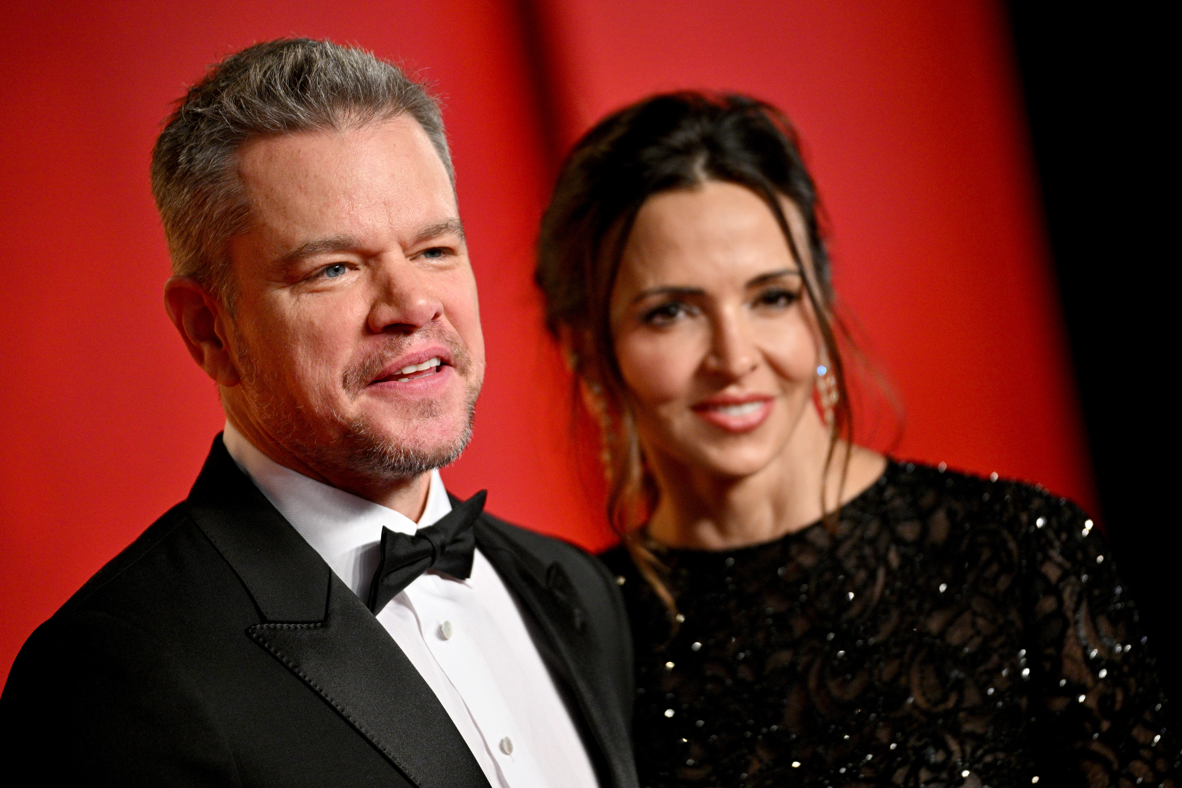 Matt Damon in a tuxedo and Luciana Barroso in a black sequined gown pose together at a red carpet event