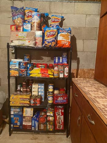 Shelving portion with assorted nutrient items including chips, cereals, pasta, canned goods, and snacks, adjacent to a woody room counter