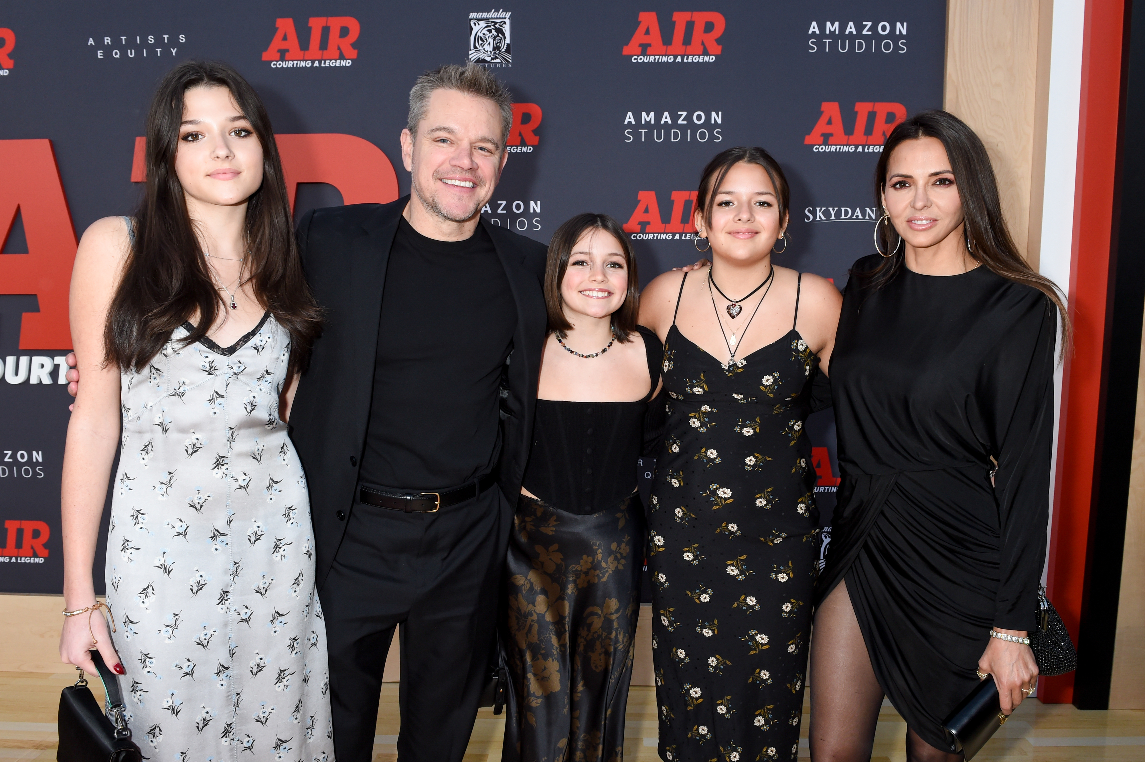 Matt Damon with his family on a red carpet at the "Air" premiere. Matt wears a black suit, his daughters and wife Luciana Barroso wear stylish, elegant dresses