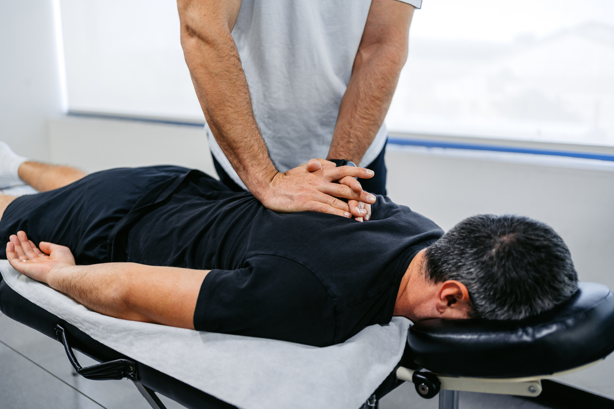 A person is receiving a back massage on a massage table. The masseuse's hands are placed on the person's back, providing therapy. No names are provided
