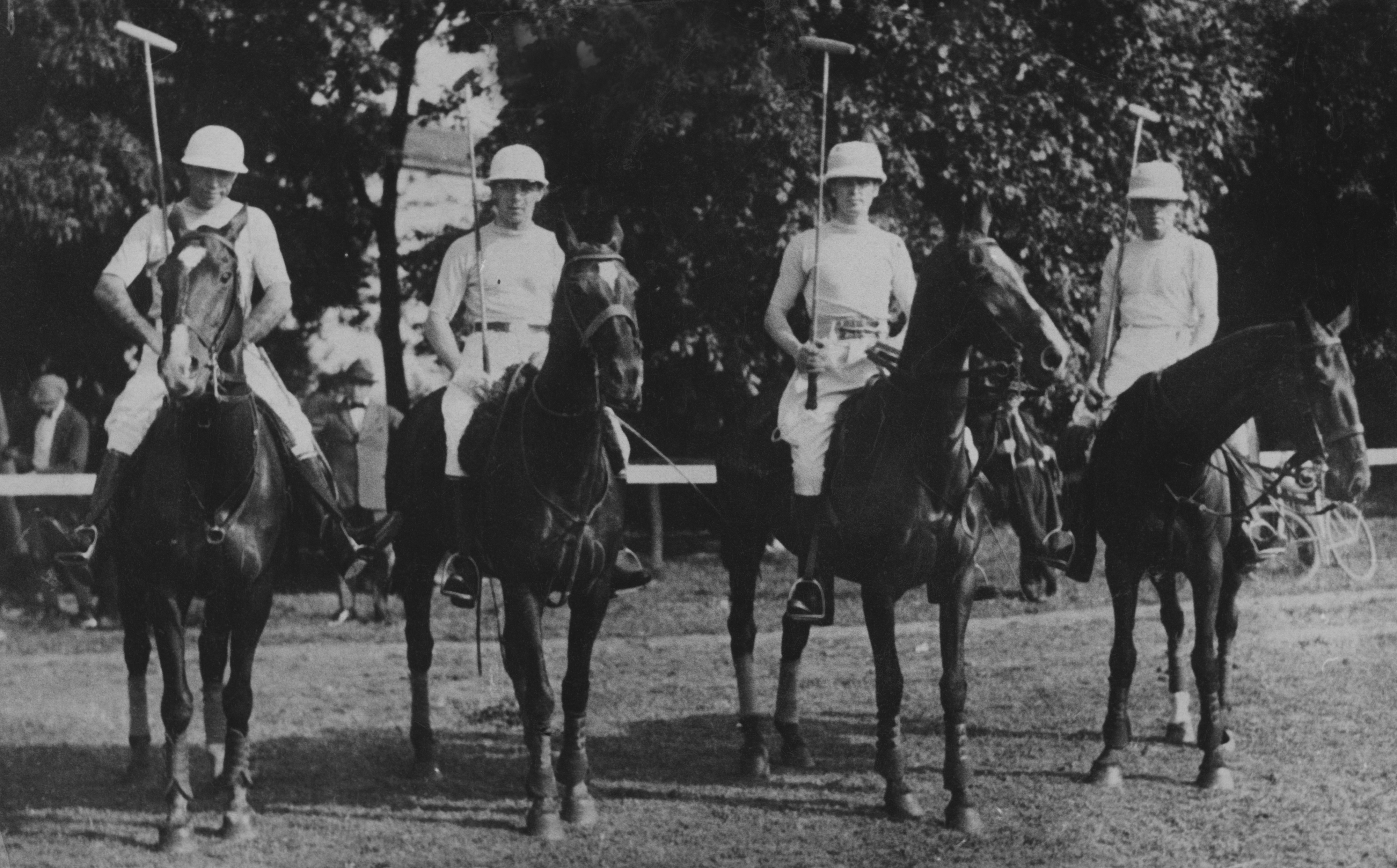 People on horseback ready to play polo, holding mallets and wearing helmets. Names of individuals are not provided