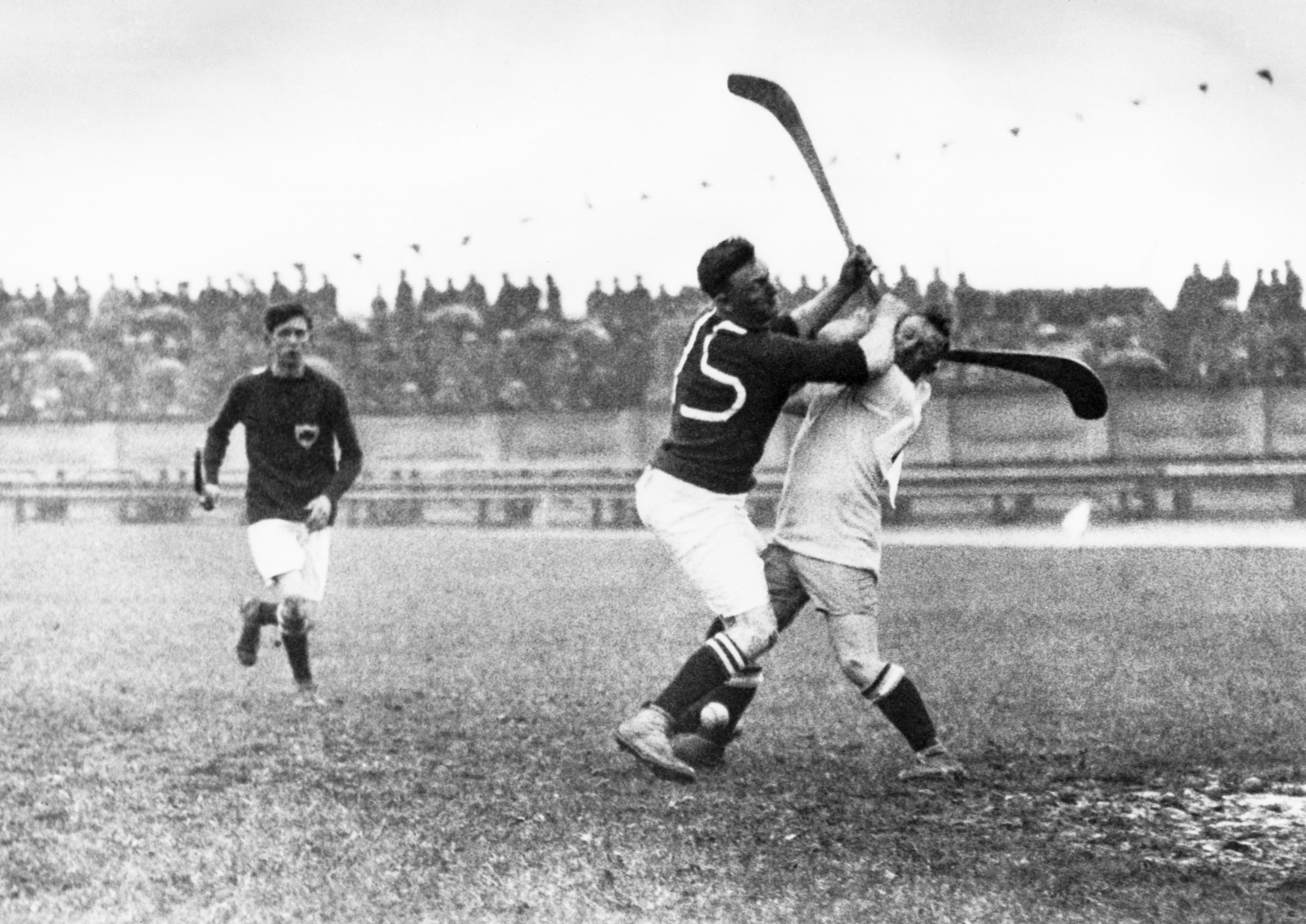 Vintage photo of a field hockey match where two players are clashing, with one player raising their stick over another's head. Another player is in the background