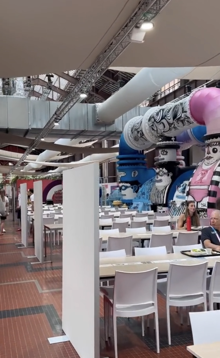 People dining in a brightly decorated restaurant with large colorful cartoon-like inflatable sculptures in the background