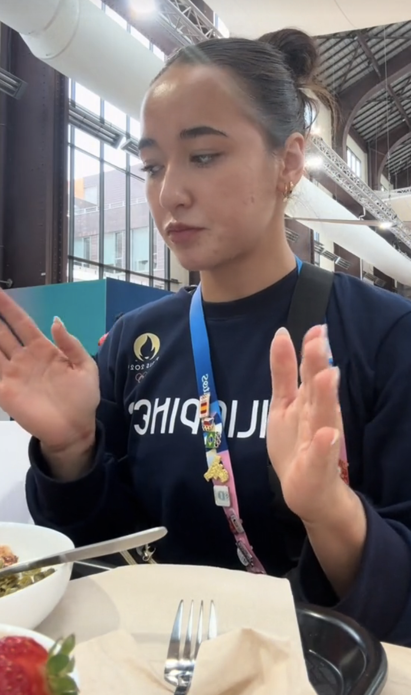 A woman in a navy shirt with "CHIP" partially visible on it, sitting at a table with food in front of her, gesturing with her hands