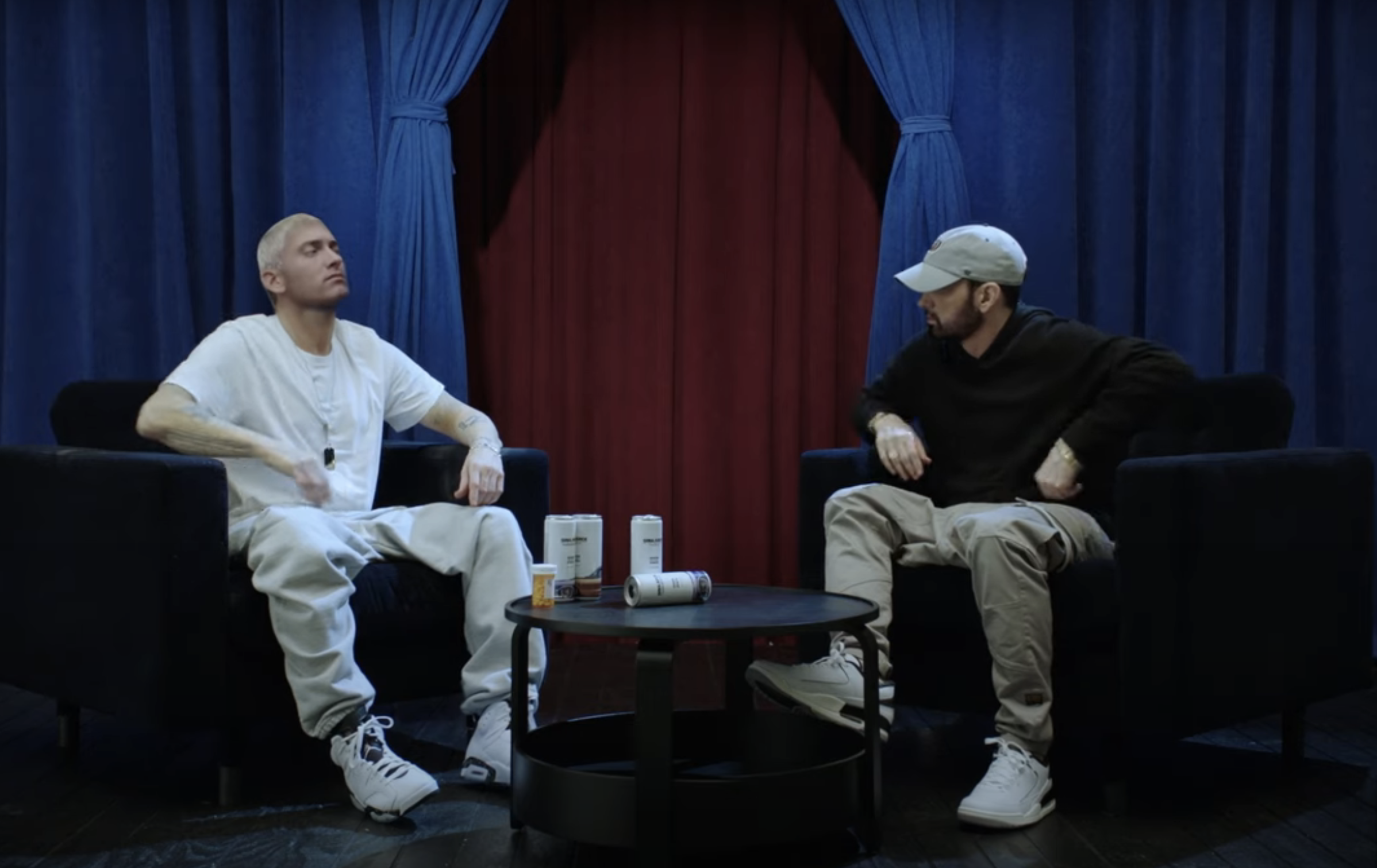 M&amp;amp;M and Eminem sit opposite each other on chairs with a small table between them holding some cans and bottles