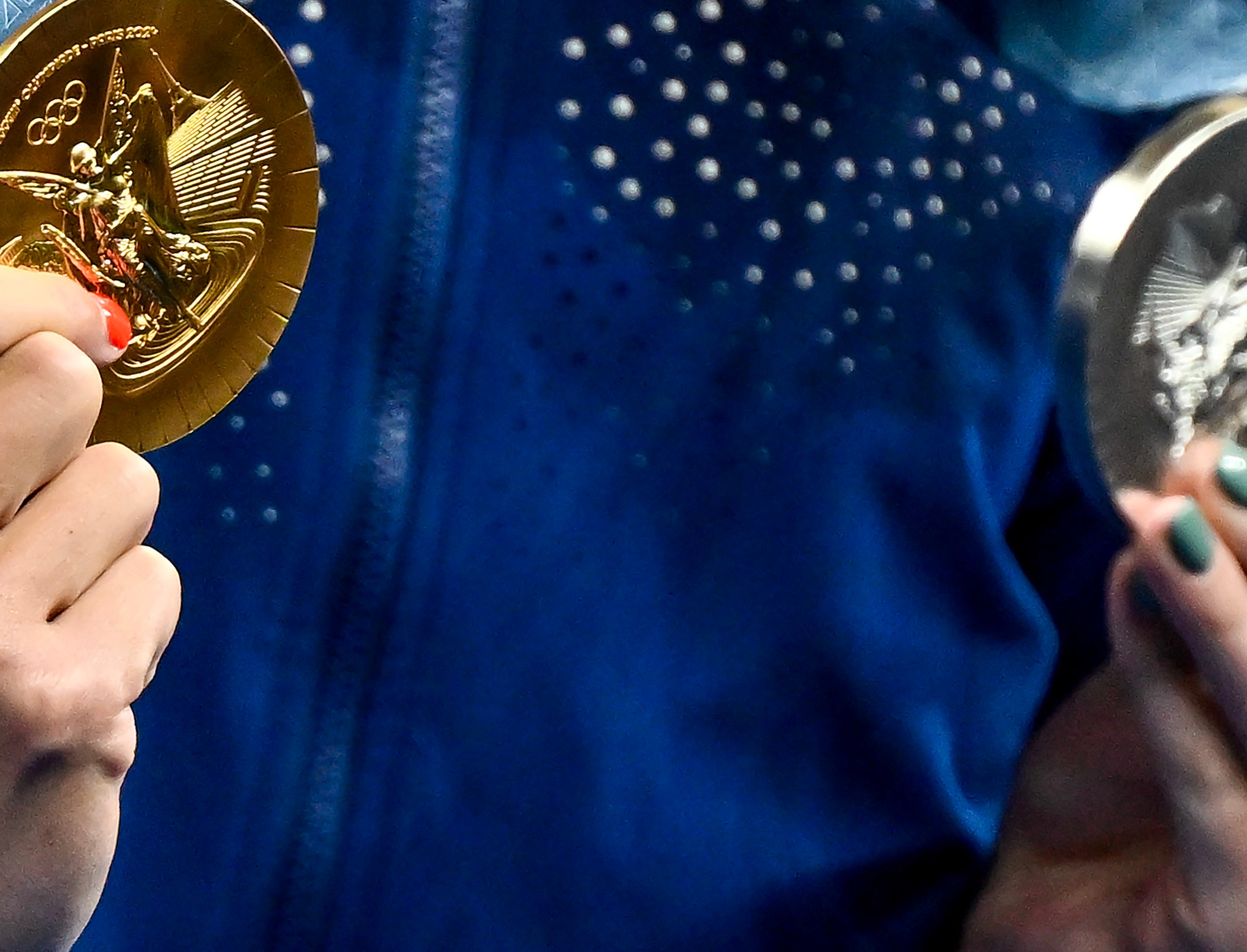 Close-up of a person's hand holding an Olympic gold medal