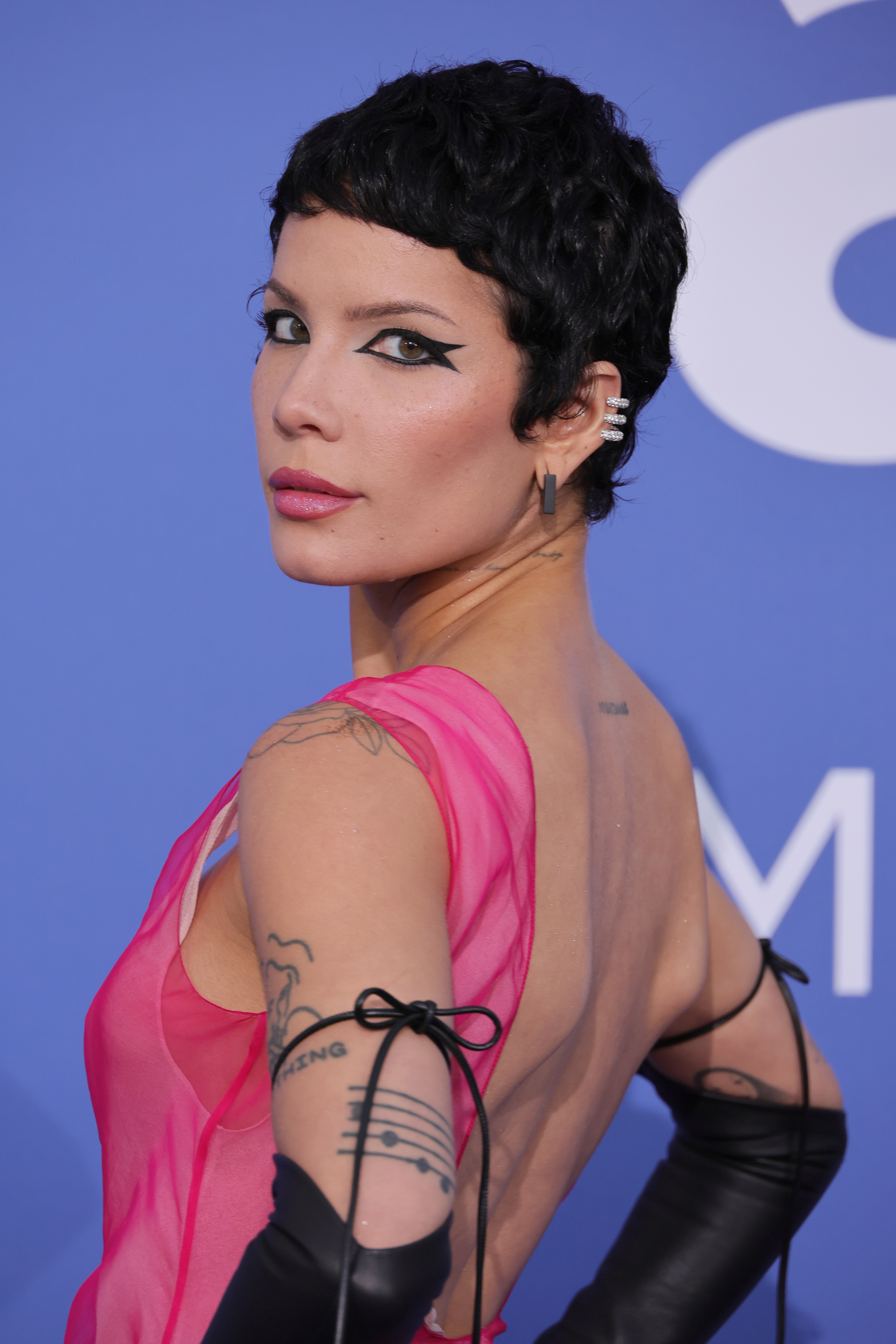 Halsey poses on the red carpet in a sheer, backless dress with black gloves and bold eyeliner