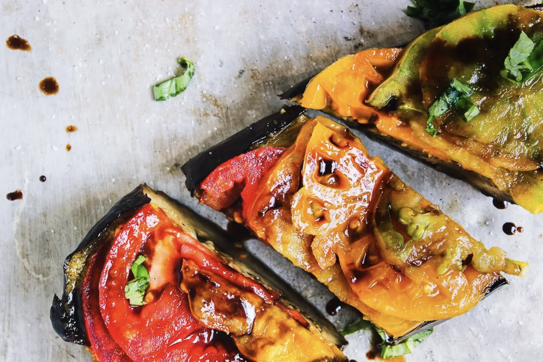 Close-up of grilled vegetable slices, including eggplant, red bell pepper, and yellow bell pepper, garnished with fresh herbs