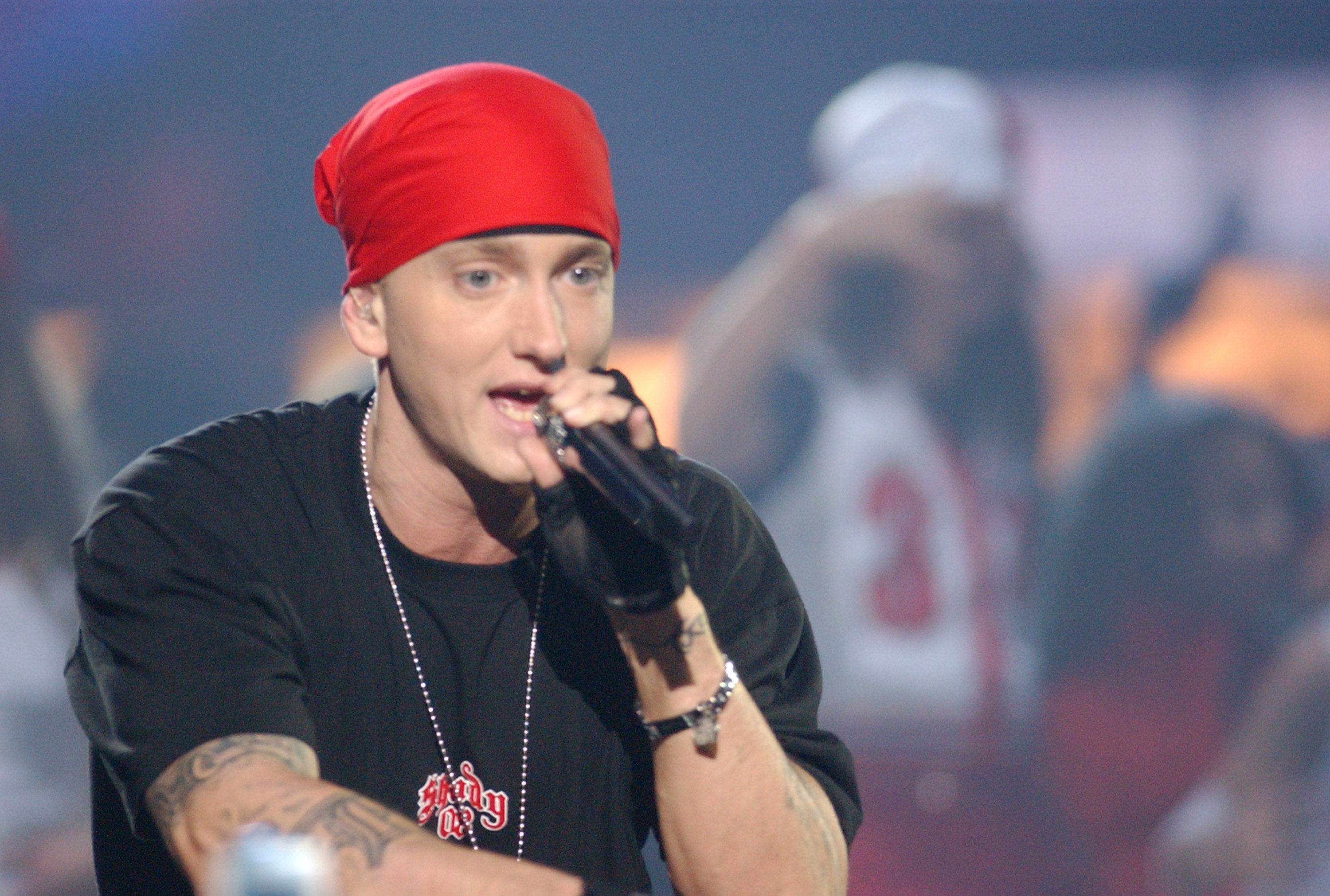 Eminem performs on stage, wearing a red bandana, black shirt, and gloves, holding a microphone