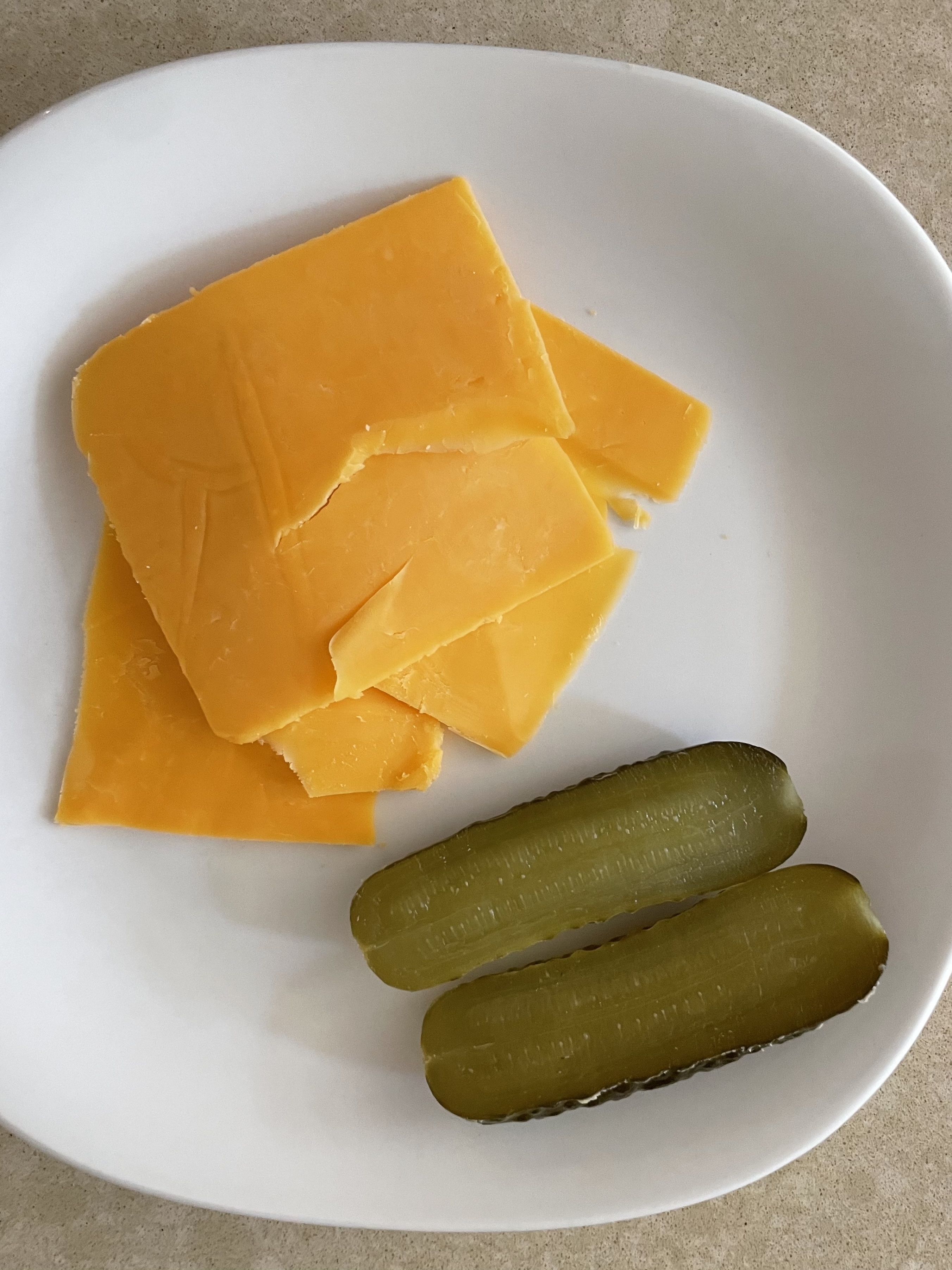 Slices of cheddar cheese and two halves of a pickle on a white plate