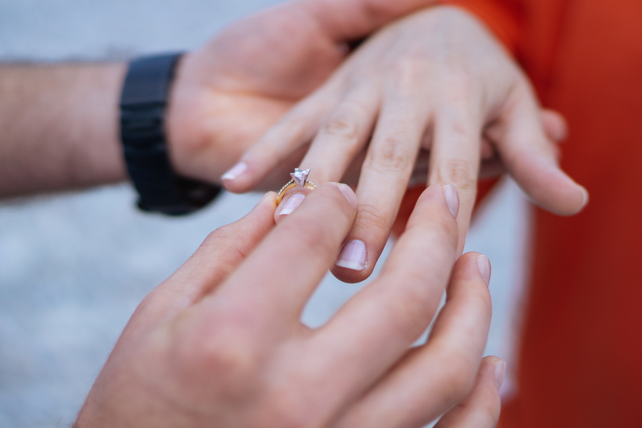 Close-up of a person's hand with an engagement ring being placed on their ring finger by another person