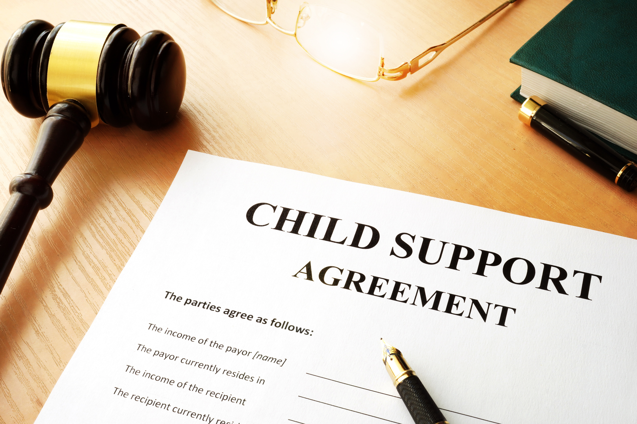 A document titled "Child Support Agreement" lies on a table next to a gavel, glasses, and a book. The agreement appears ready for signatures