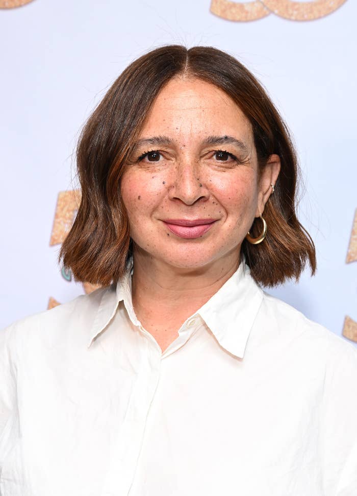 Maya Rudolph smiles, wearing a white collared shirt and gold hoop earrings