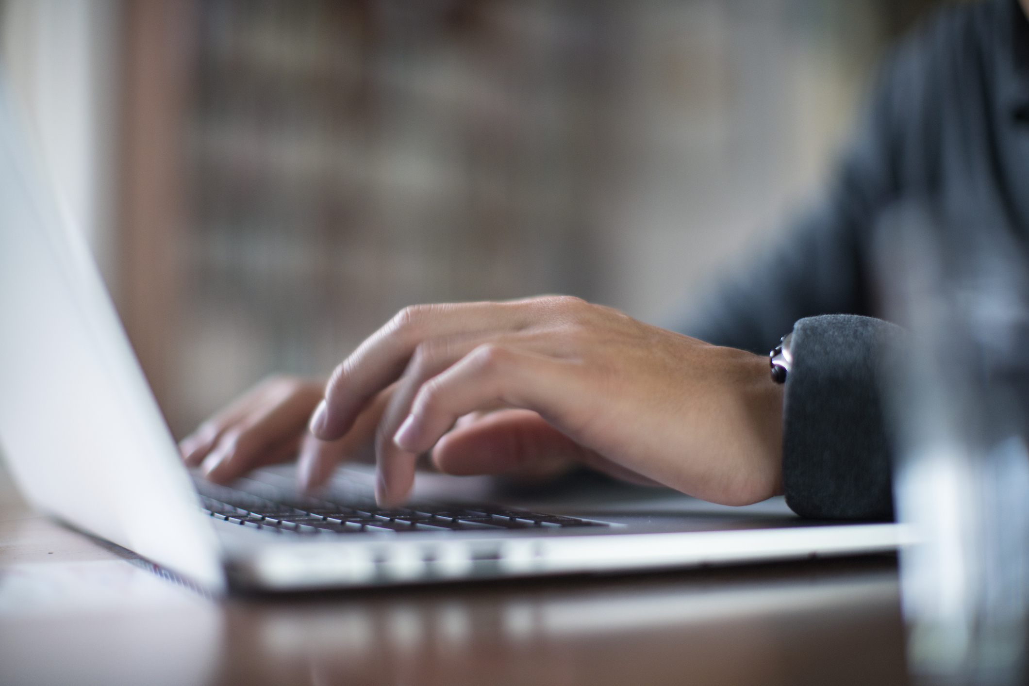 Close-up of person's hands typing on a laptop keyboard