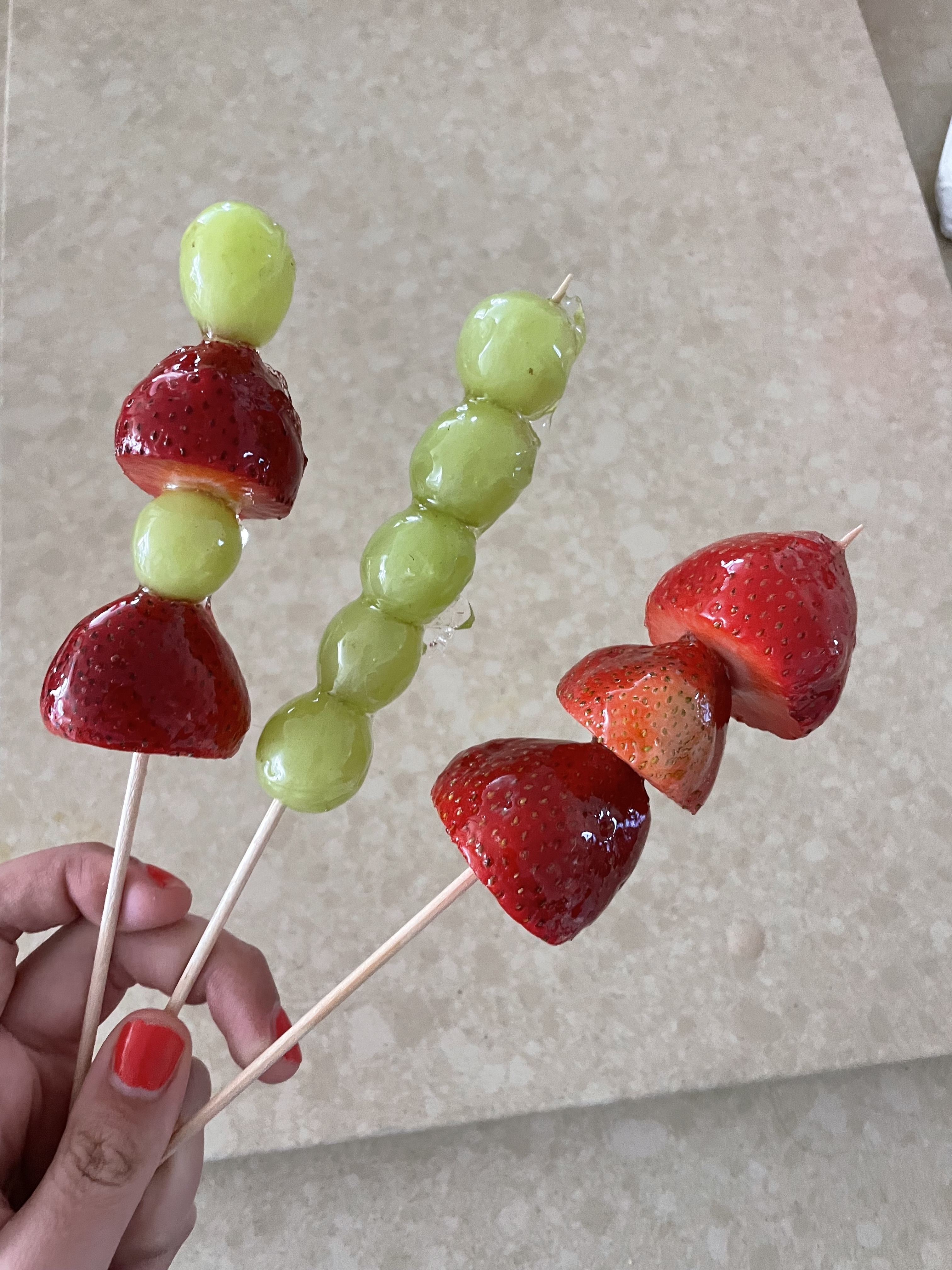 Three fruit skewers held up, each with different combinations of strawberries and green grapes on wooden sticks
